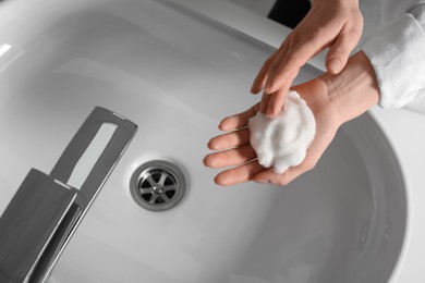Photo of Woman washing hands with cleansing foam near sink in bathroom, closeup