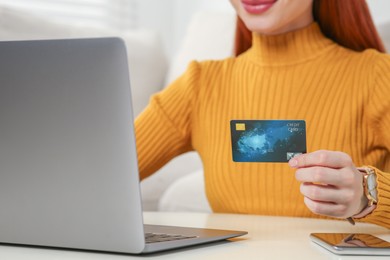 Woman with credit card using laptop at white table indoors, closeup