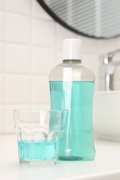 Photo of Bottle of mouthwash and glass on white table in bathroom