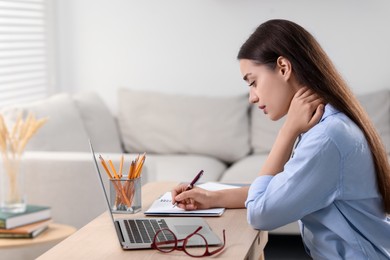 Photo of Young woman suffering from neck pain while working at table in office