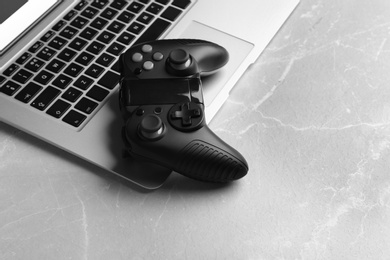 Photo of Video game controller and laptop on grey table. Space for text