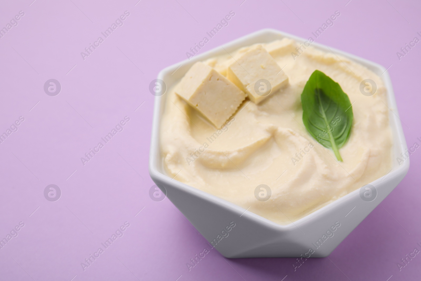 Delicious tofu sauce and basil leaf in bowl on violet background, closeup. Space for text Photo of Delicious tofu sauce and basil leaf in bowl on violet background, closeup. Space for text