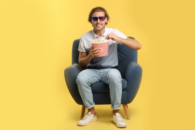 Photo of Emotional man with 3D glasses and popcorn sitting in armchair during cinema show on color background