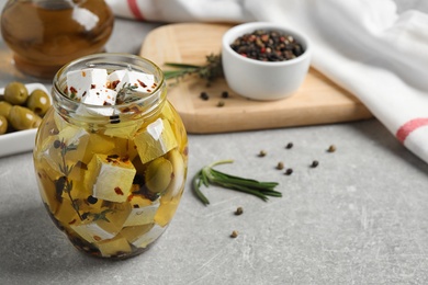 Photo of Jar with feta cheese marinated in oil on light grey table. Pickled food