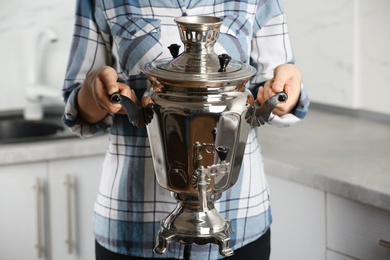 Photo of Woman holding metal samovar in kitchen, closeup. Russian tea culture