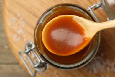 Photo of Jar and spoon with tasty salted caramel on table, top view