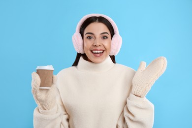 Photo of Beautiful young woman in earmuffs with cup of drink on light blue background