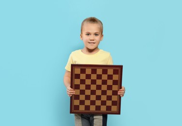 Cute girl holding chessboard on light blue background