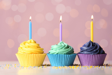 Photo of Delicious birthday cupcakes with cream and burning candles on table