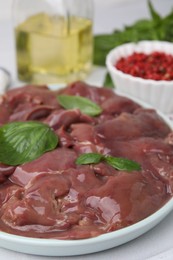Photo of Plate of raw chicken liver with basil on white table, closeup