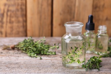 Photo of Thyme essential oil and fresh plant on wooden table, space for text