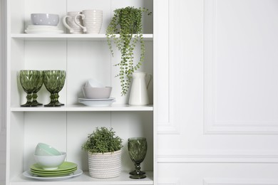 Photo of Different clean dishware and houseplants on shelves in cabinet indoors