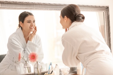 Photo of Beautiful young woman looking at herself in mirror indoors