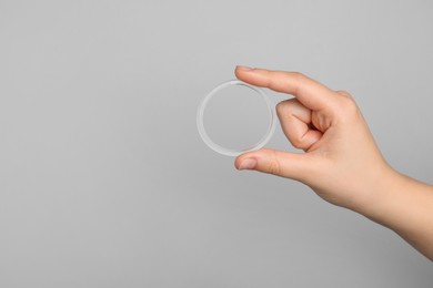 Photo of Woman holding diaphragm vaginal contraceptive ring on grey background, closeup. Space for text
