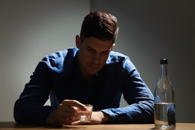Photo of Addicted man with alcoholic drink at wooden table indoors
