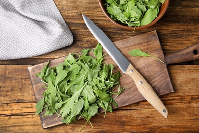 Photo of Cutting board with fresh arugula leaves and knife on wooden table, flat lay