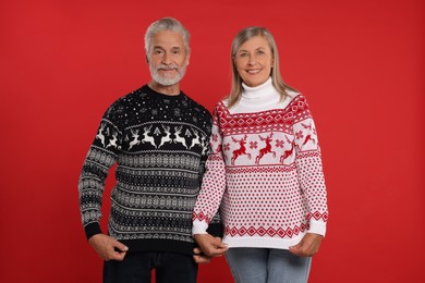 Photo of Senior couple showing Christmas sweaters on red background