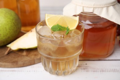 Photo of Tasty kombucha and ice cubes in glass on white wooden table, closeup