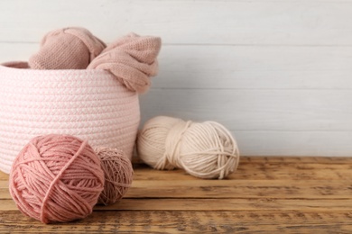 Photo of Woolen yarns in basket on wooden table. Space for text