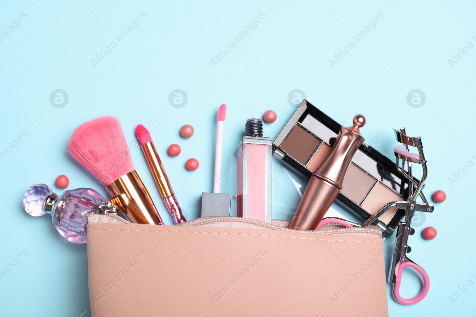 Photo of Cosmetic bag and makeup products with accessories on light blue background, flat lay