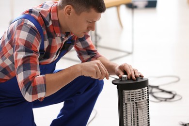 Photo of Professional technician repairing electric halogen heater with screwdriver indoors