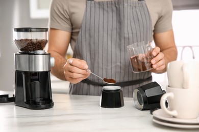 Photo of Man putting ground coffee beans into moka pot at table in kitchen, closeup