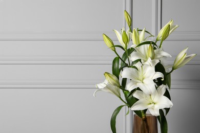 Photo of Beautiful bouquet of lily flowers in glass vase near light grey wall, space for text