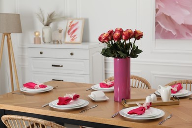 Color accent table setting. Plates, cutlery, pink napkins and vase with beautiful roses in dining room