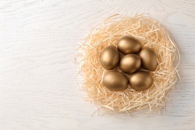 Photo of Golden eggs in nest on wooden background, top view with space for text