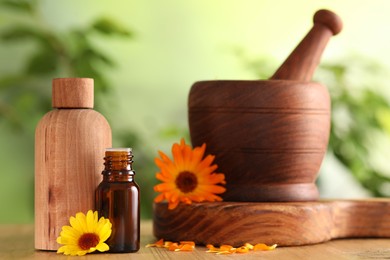 Photo of Bottles of essential oils, mortar and beautiful calendula flowers on wooden table outdoors