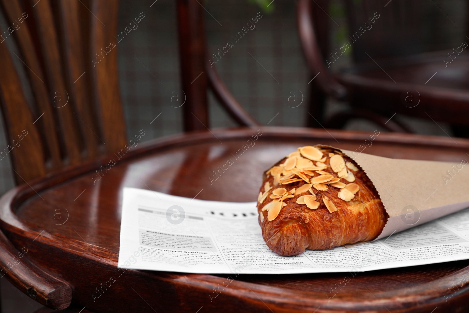 Photo of Delicious croissant in paper bag on wooden chair, space for text