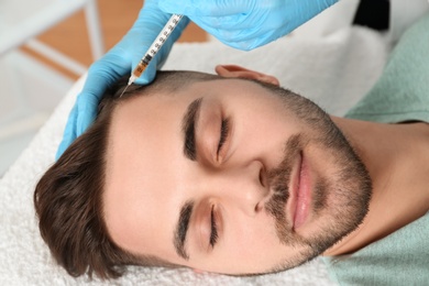 Photo of Young man with hair loss problem receiving injection in salon, closeup