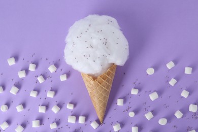Photo of Sweet cotton candy in waffle cone and marshmallows on purple background, flat lay