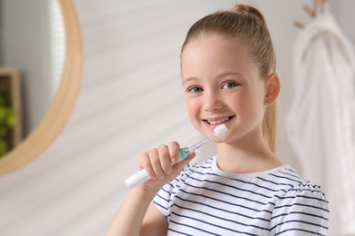 Photo of Cute little girl brushing her teeth with electric toothbrush in bathroom, space for text