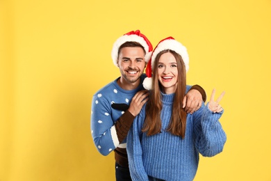 Photo of Couple wearing Christmas sweaters and Santa hats on yellow background