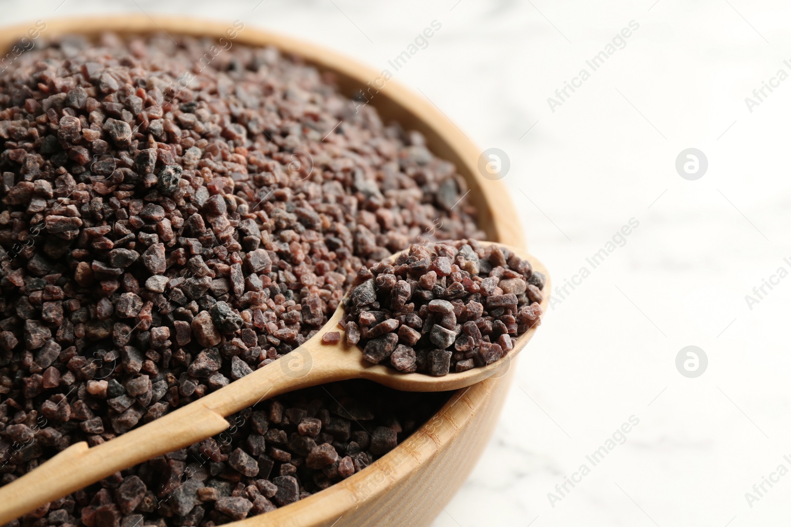 Photo of Black salt in bowl with spoon on white table, closeup. Space for text