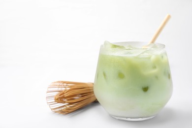 Photo of Glass of tasty iced matcha latte and bamboo whisk on white tiled table, closeup. Space for text
