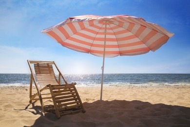 Photo of Deck chair near red and white striped beach umbrella on sandy seashore