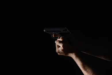 Photo of Professional killer with gun on black background, closeup