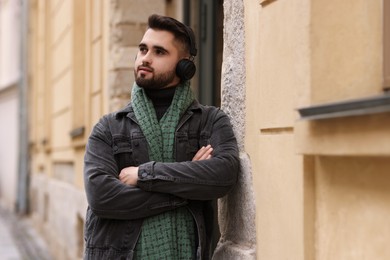 Photo of Handsome man in warm scarf and headphones near building outdoors