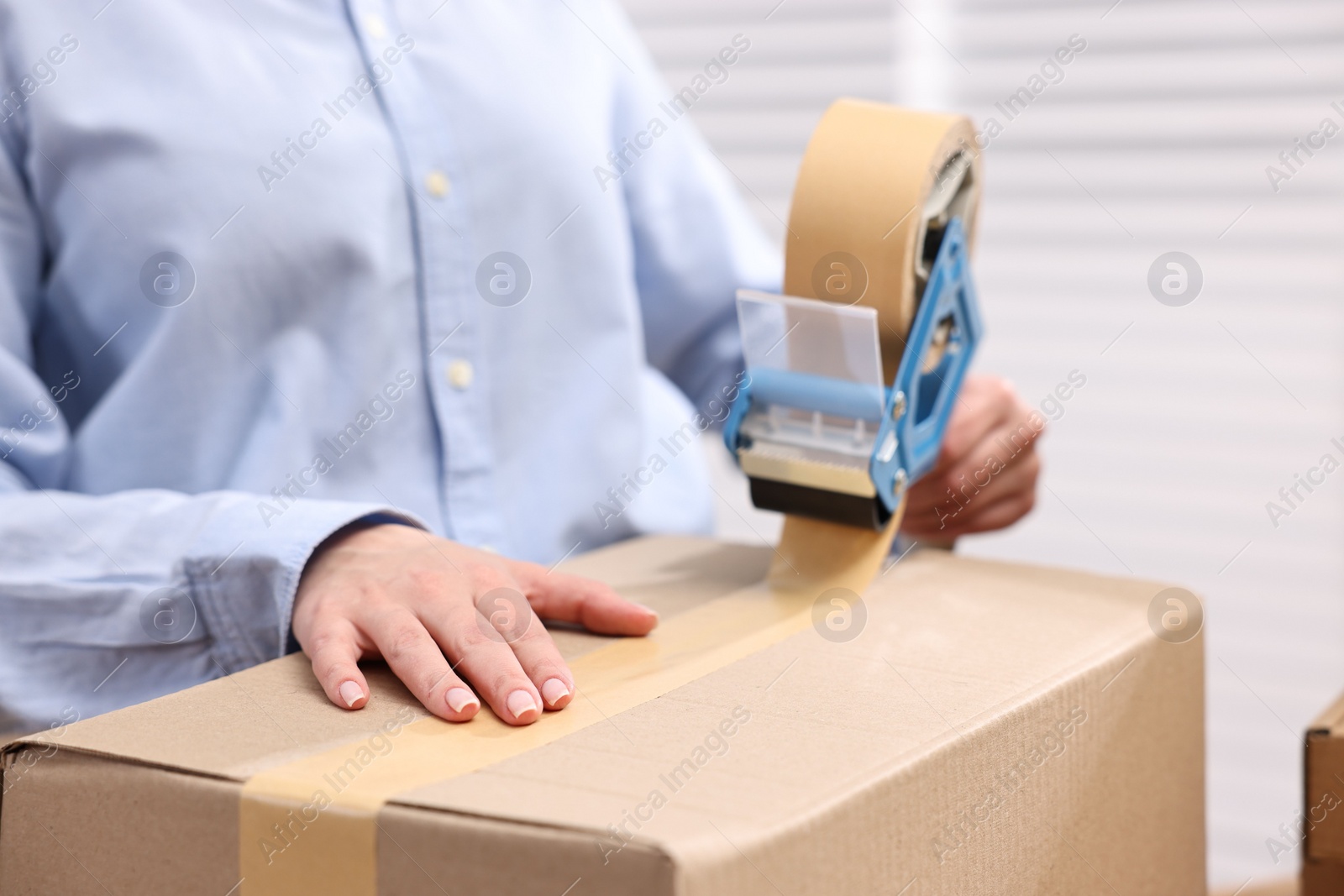 Photo of Parcel packing. Post office worker taping box indoors, closeup