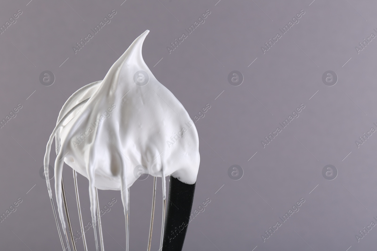 Photo of Whisk with whipped cream on grey background, closeup. Space for text