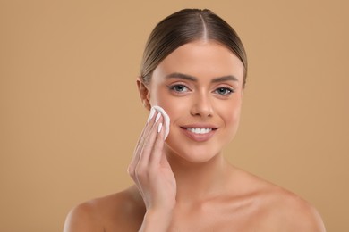 Photo of Beautiful woman removing makeup with cotton pad on beige background