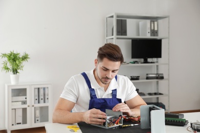 Photo of Male technician repairing power supply unit at table indoors