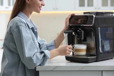 Photo of Young woman preparing fresh aromatic coffee with modern machine in kitchen, closeup