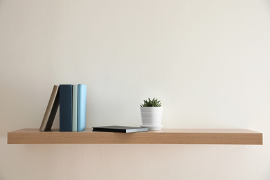 Photo of Wooden shelf with books and houseplant on light wall