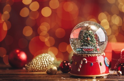 Photo of Beautiful snow globe with Christmas tree on wooden table against blurred festive lights. Space for text