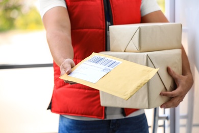 Photo of Young courier holding parcels on doorstep, closeup. Delivery service