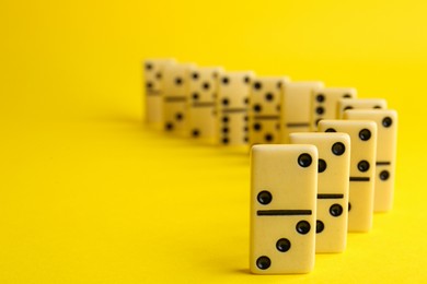 Photo of Row of white domino tiles on yellow background. Space for text