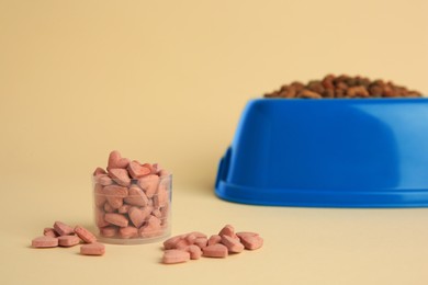 Photo of Vitamins and dry pet food in bowl on beige background, space for text